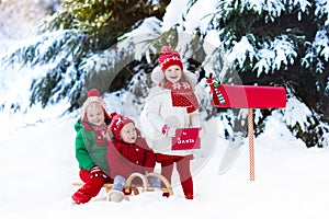 Children with letter to Santa at Christmas mail box in snow