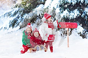 Children with letter to Santa at Christmas mail box in snow