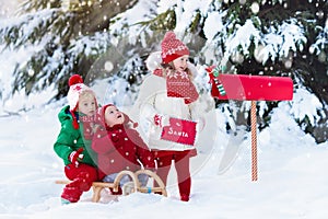 Children with letter to Santa at Christmas mail box in snow