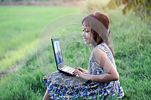 Happy children learning outdoor by studying online and working on laptop in green field