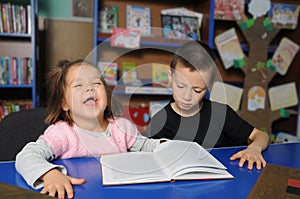 Happy children in library interesting reading book. Little girl and boy together learning