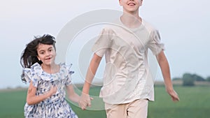 Happy children. A little girl and a teenage boy are running across a field holding hands.