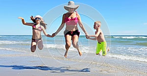 Happy children and mom jump on the beach in a sunny day of summer