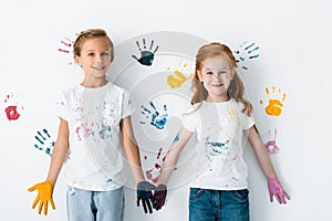 happy children with paint on hands standing near colorful hand prints on white.