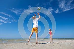 Happy children playing with ball on beach at summer sunny day with blue sky