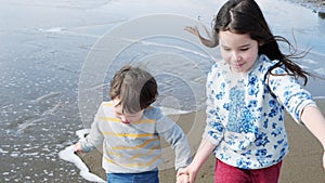 Happy children playing on the beach. Sister and her little brother run holding hands