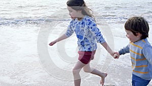 Happy children playing on the beach. Sister and her little brother run holding hands