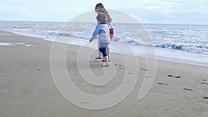 Happy children playing on the beach. Sister and her little brother run holding hands