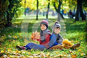 Happy children playing in beautiful autumn park on warm sunny fall day. Kids play with golden maple leaves