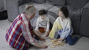 Happy children playing wooden constructor on the floor with grandad