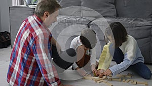 Happy children playing wooden constructor on the floor with grandad, slow motion