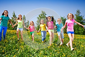 Happy children run and hold hands in green field