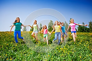 Happy children run and hold hands in green meadow