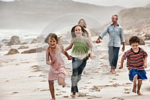 Happy children running on beach with parents walking in background