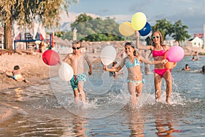 Happy children running together with balloons through the water