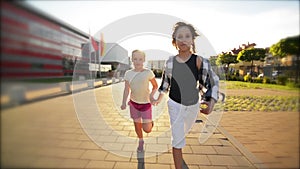 Happy Children Running Together Holding Hands On The Road. The Rays Of The Sun Shine in Their Faces.