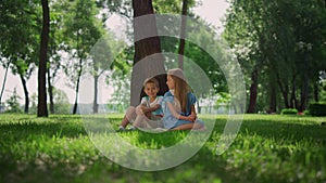 Happy children seat near tree on green grass. Cute boy girl playing on nature.