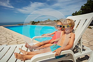 Happy children, siblings relax at resort poolside in sunny day