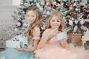 Happy children sister open magic gift home near tree in dress. Merry Christmas.