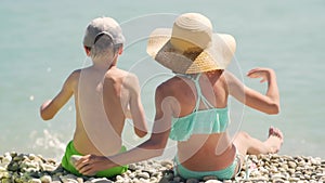 Happy children sitting on the beach near blue water at the sea. Summer vacations. Kids having fun on vacations