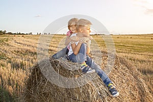 happy children sitting on haystack at sunset. girl hugged boy sitting in field