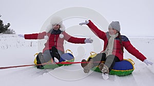 Happy children sledding in snow in the winter and waving their hands. Family plays in winter park during the Christmas