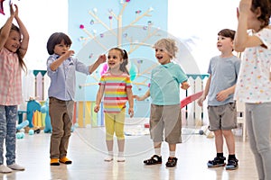 Happy children stand semicircle on floor in kindergarten or day care centre. Preschool kids having fun indoors, playing