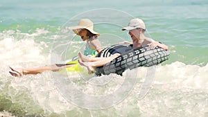 Happy children swimming in blue water at the sea. Summer vacations. Girl and boy on inflatable rings ride on breaking