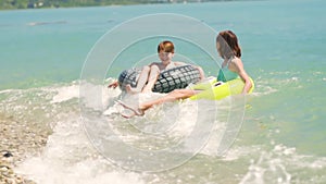 Happy children swimming in blue water at the sea. Summer vacations. Girl and boy on inflatable rings ride on breaking