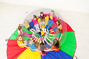 Happy children and teacher sitting on parachute