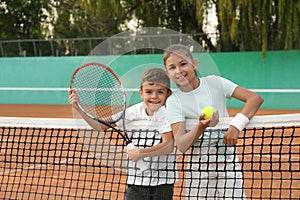 Happy children with tennis racket and ball on court outdoors