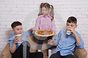 Happy children, two boys and a girl, are holding a big italian pizza, emotions and smiles, concept