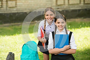 Happy children in uniform hold school books for doing homework assignment outdoors, education