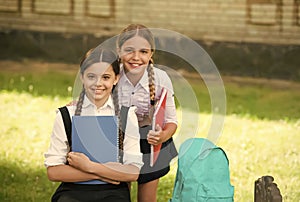 Happy children in uniform hold school books for doing homework assignment outdoors, education