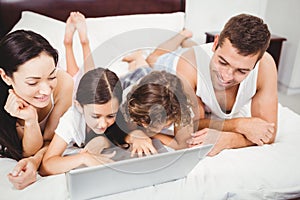 Happy children using laptop with parents on bed at home