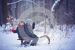 Happy children in a winter park, playing together with a sledge