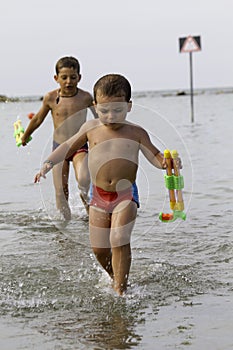 Happy childs play into sea with watergun, vacation in Italy