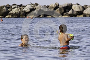 Happy childs play into sea with watergun, vacation in Italy