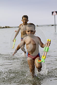 Happy childs play into sea with watergun, vacation in Italy