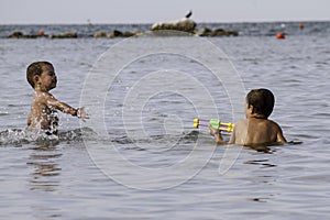 Happy childs play into sea with watergun, vacation in Italy