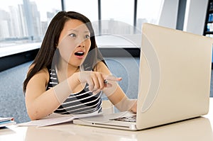 Happy chinese asian woman working and studying on her computer sitting at modern office desk smiling cheerful