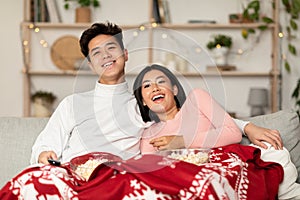 Happy Chinese Couple Watching TV Sitting On Couch At Home