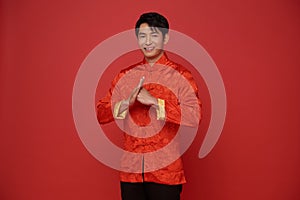 Happy Chinese new year 2024. Asian man wearing red traditional clothing with gesture of congratulation isolated on red background