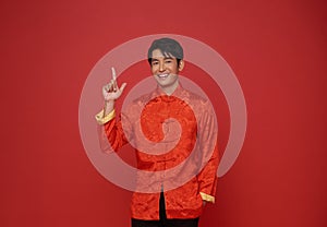 Happy Chinese new year 2024. Asian man wearing red traditional costume and hands pointing finger up isolated on red copy space