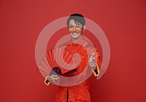 Happy Chinese new year 2024. portrait Asian man happy smile wearing red traditional clothing holding red fan and pointing