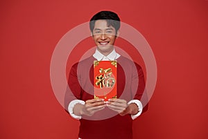 Happy Chinese new year. Asian man holding angpao or red packet monetary gift isolated on red background. Chinese text means great