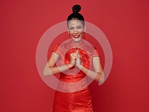 Happy Chinese new year. Asian woman wearing traditional cheongsam qipao dress with gesture of congratulation isolated on red