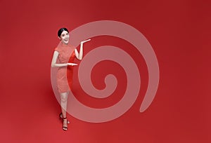 Happy Chinese new year. Asian woman wearing traditional cheongsam qipao dress with gesture of welcome isolated on red copy space