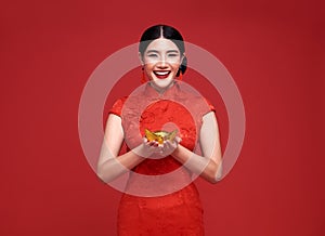 Happy Chinese new year. Asian woman wearing traditional cheongsam qipao dress holding gold ingot isolated on red background