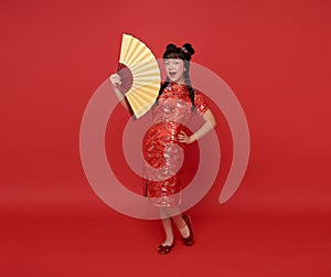 Happy Chinese new year. children asian girl wearing traditional cheongsam qipao dress holding fan isolated on red background